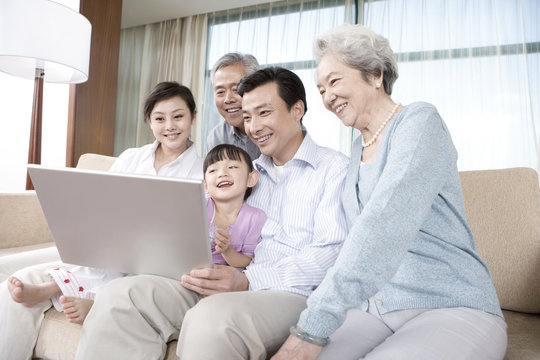 Grandparents and Parents with daughter look at Laptop on a sofa
