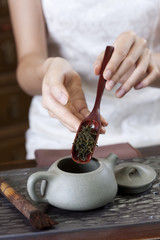 Fototapeta na wymiar Young woman putting tea leaves into teapot