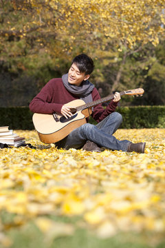 Male college student with guitar and books enjoying the charming natural beauty in the autumn