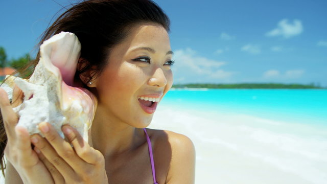Ethnic Asian Chinese female holding conch shell on beach