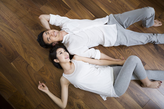 Young couple holding hands lying on wooden floor 