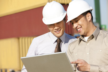 businessman with shipping industry worker looking over a laptop