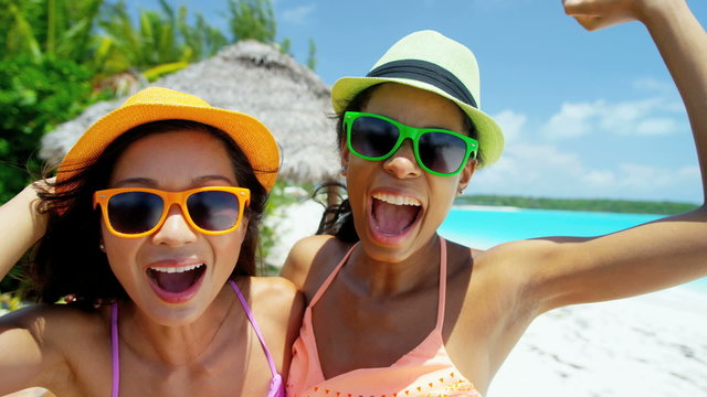 Multi ethnic girlfriends wearing bikini and hat filming beach selfie 