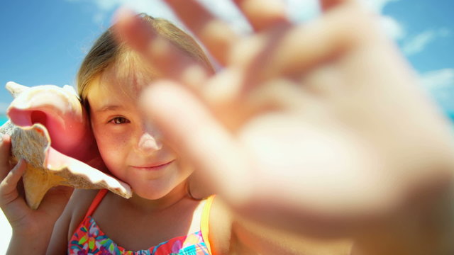 Portrait of cute smiling Caucasian girl on tropical beach holding conch shell