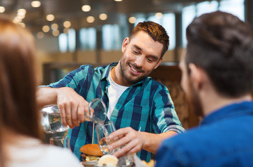 happy man with friends pouring water at restaurant