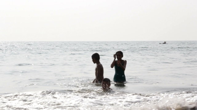 Teenage kids playing with the sea waves breaking at seashore in the tropical sea