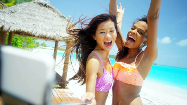 Smiling multi ethnic girls taking selfie on tropical beach