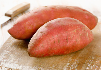 Raw sweet potatoes on a wooden background .