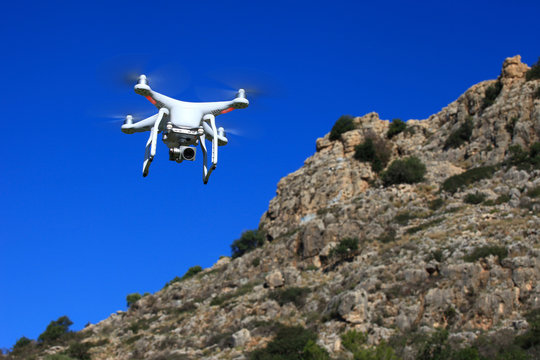White drone equipped with high resolution 4K video camera hovering in mid air with a blurred cliff in the background