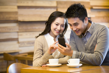 Happy young couple with smart phone in cafe
