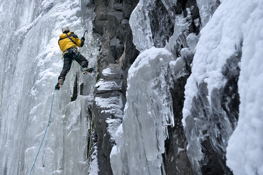 Bergsteiger klettert mit Eisgeräten und Steigeisen einen gefrorenen Wasserfall hinauf. Sicherung an Eisschrauben mit Doppelseiltechnik.