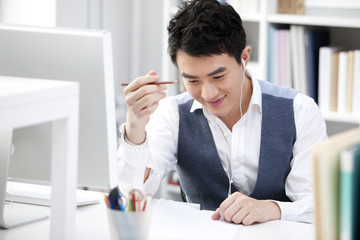 Naklejka premium Happy young businessman with earbuds in the office