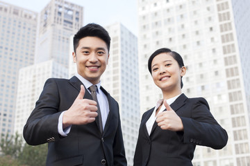Cheerful young business partners doing thumbs up in downtown district