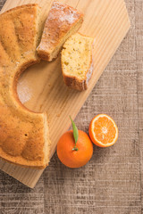 Slices of clementine cake with powdered sugar topping. Cake on a board with fresh clementines on wooden board.