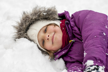 Tired little girl, laying in the snow and smiling.