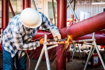 Worker cutting steel red pipe with acetylene welding cutting torch. Industrial construction site background.