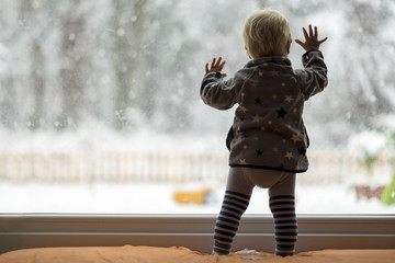 Toddler child standing in front of a big window leaning against