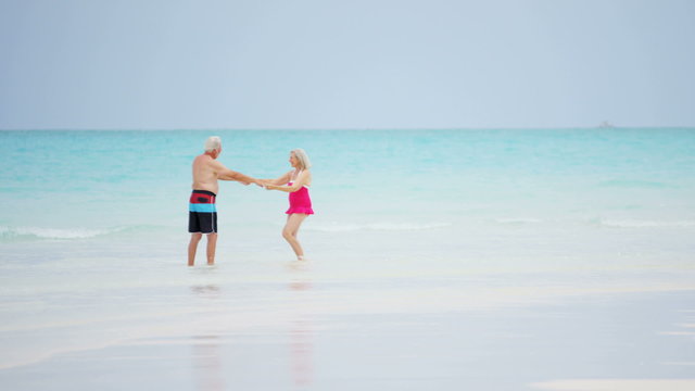 Caucasian senior couple dancing outdoor on a vacation beach in swimwear 