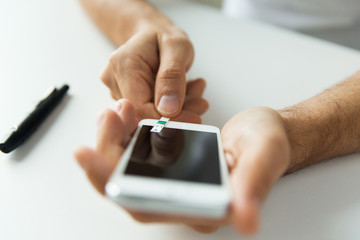 close up of man with smartphone making blood test