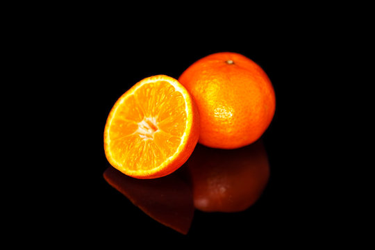Three tangerines lie on a black mirror.