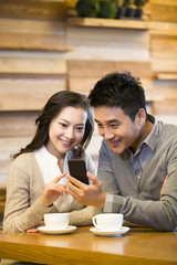 Happy young couple with smart phone in cafe