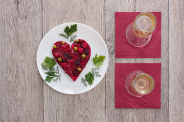 Beetroot and vegetables salad made in hearth shape served with herbs on plate with two glasses of champagne against wooden background