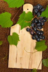 Grape with vine leaves with empty cutting board background. Selective focus on board.