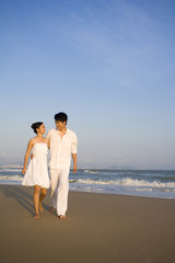 Fototapeta na wymiar Young couple in white walking along the beach