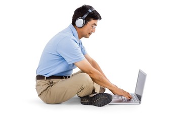 Side view of man listening music while using laptop