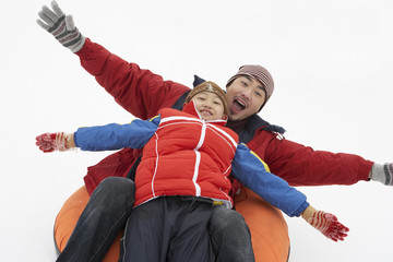 Father And Son Riding On Inflatable Snow Tube