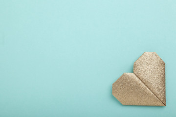 Gold glitter origami heart on turquoise paper background
