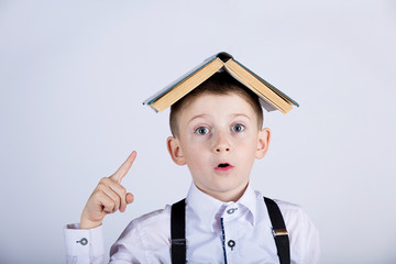 Surprised, cute little schoo boy with a open book on her head, isolated over yellow background.