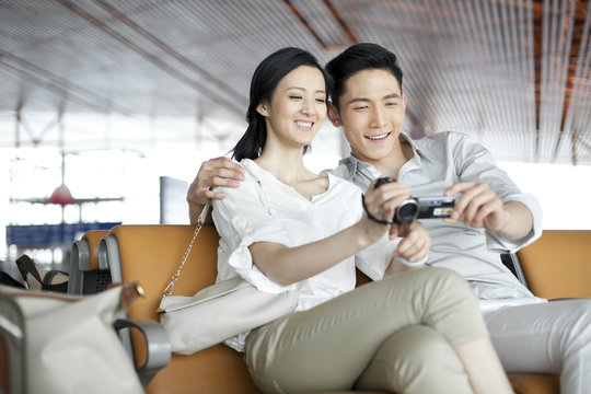 Young couple using camcorder in airport lounge