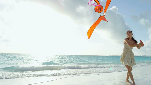 Smiling Asian Chinese girl playing with red kite on beach vacation