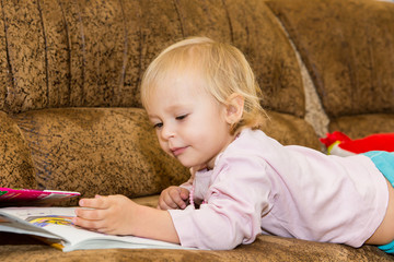 A small child - a girl paints a picture lying on the couch at home