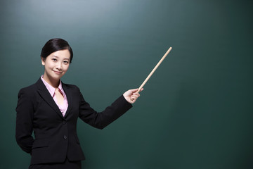 Happy female teacher holding teacher's pointer in classroom