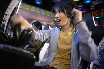Fototapeta na wymiar Teenagers Playing Racing Games At Arcade