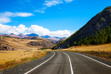 Landscape with rural asphalt road through the prairie and the mountains clouds in summer day