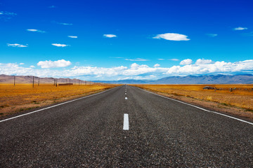 Landscape with rural asphalt road through the prairie and clouds on blue sky in summer day