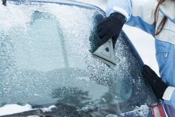 Beautiful young woman removing snow from her car.