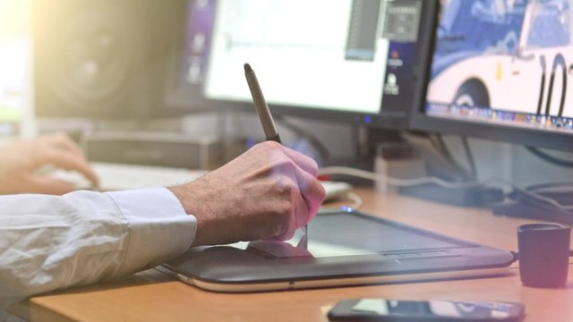 Graphic Designer working with digital Drawing tablet and Pen on a computer. Smooth tracking shot with nice backlit lensflare.