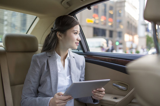 Businesswoman using digital tablet in car back seat