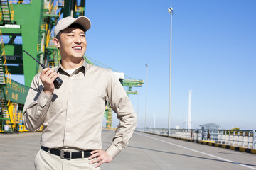 Male shipping industry worker with walkie talkie and crane in the background