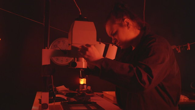 Photographer using photographic enlarger to produce prints from film in darkroom