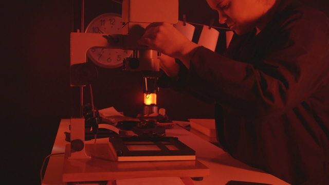 Female photographer working in red darkroom adjusting the enlarger