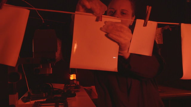 Woman photographer working in darkroom with photographs hanging to dry
