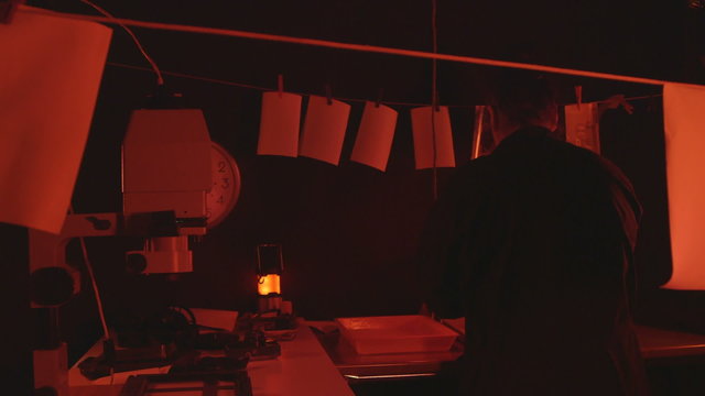 Woman photographer working in darkroom with photographs hanging to dry