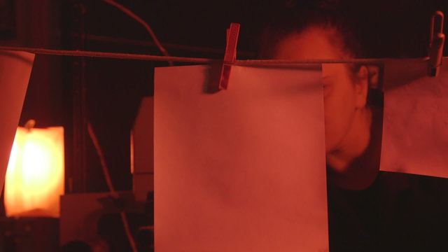 Woman photographer working in darkroom with photographs hanging to dry
