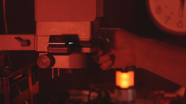 Man photographer using enlarger in red darkroom to produce photographic prints