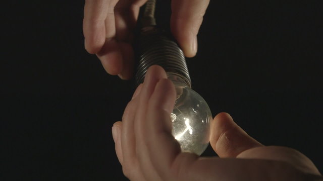 Hand installing electric light bulb in dark room